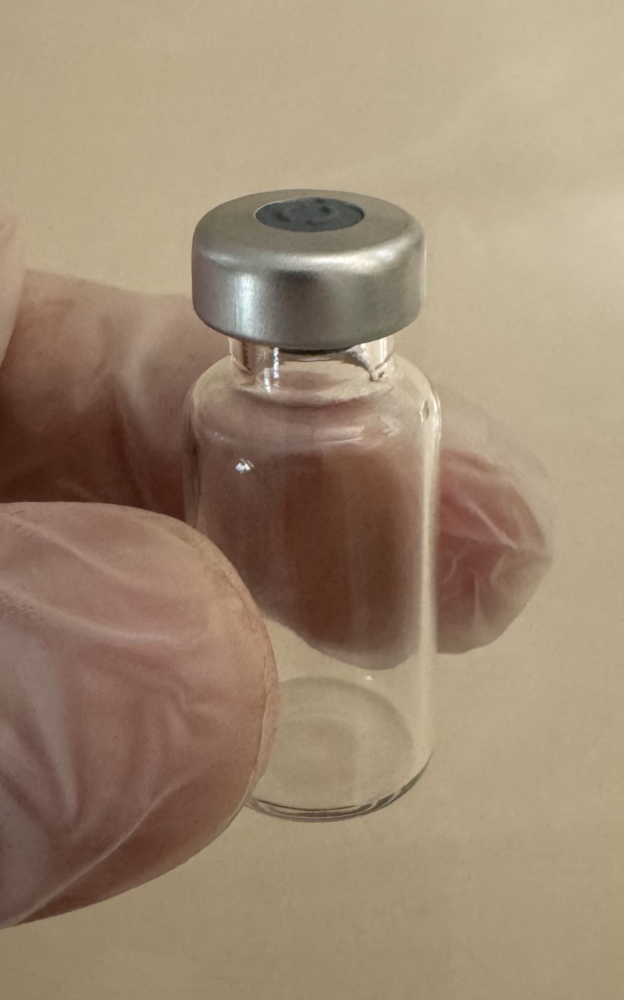 Empty glass vial with crimp cap, held in a gloved hand