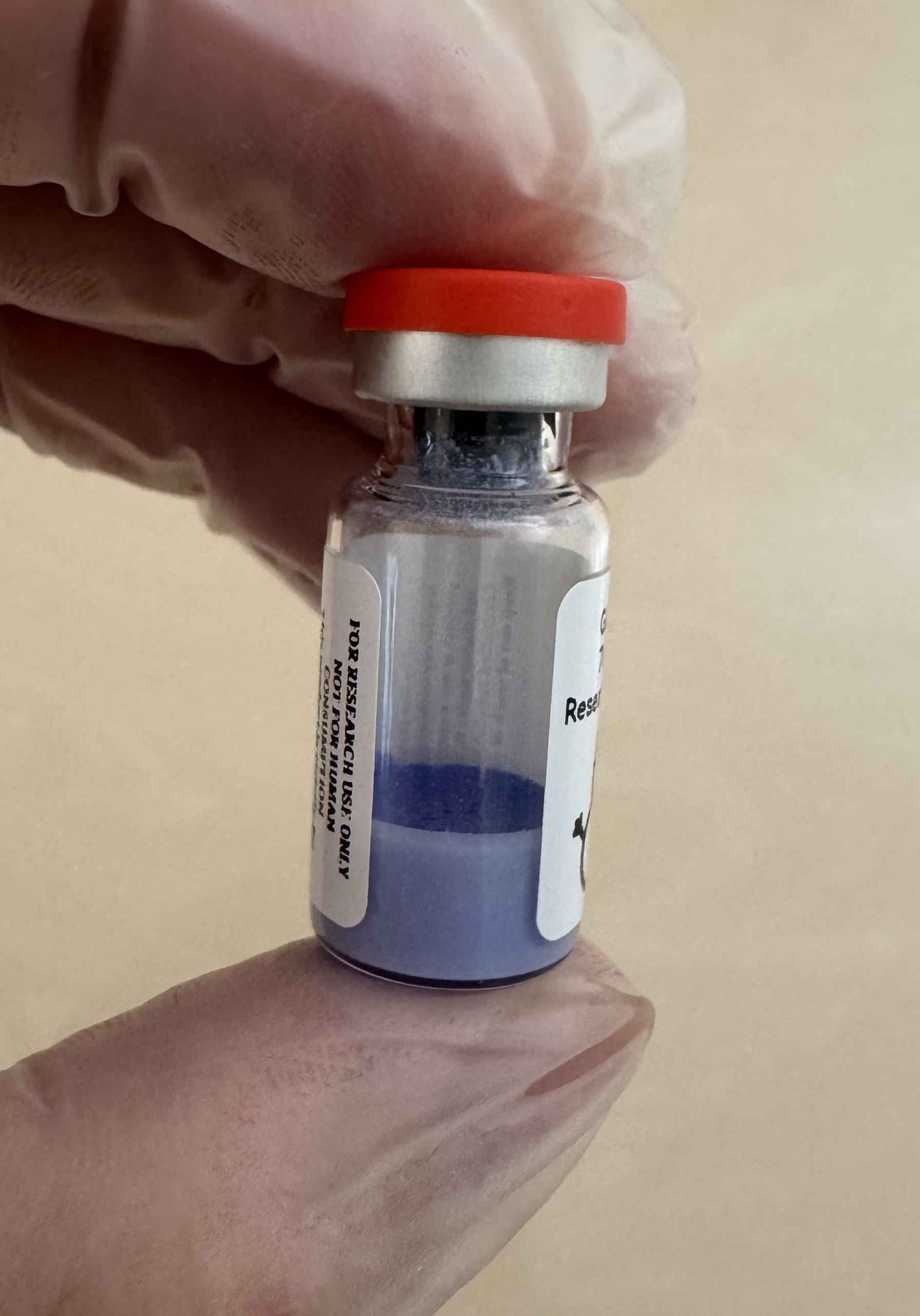 Blue lyophilized GLOW (GHK-Cu + BPC-157 + TB-500) 70mg powder cake inside the sealed vial